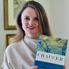 Smiling woman faces camera. She is holding a copy of her book 'Chaucer; A European Life', is against a white background, and is wearing a cream jumper